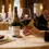 Tangan elegan memegang batang gelas wine kristal berisi red wine di meja restoran mewah dengan pencahayaan hangat lilin