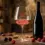 Gelas kristal Burgundy berisi wine Pinot Noir merah ruby transparan di samping botol klasik dan buah ceri
