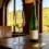 Gelas kristal berisi wine Riesling kuning keemasan segar dengan botol hijau khas Jerman di atas meja kayu berlatar kebun anggur